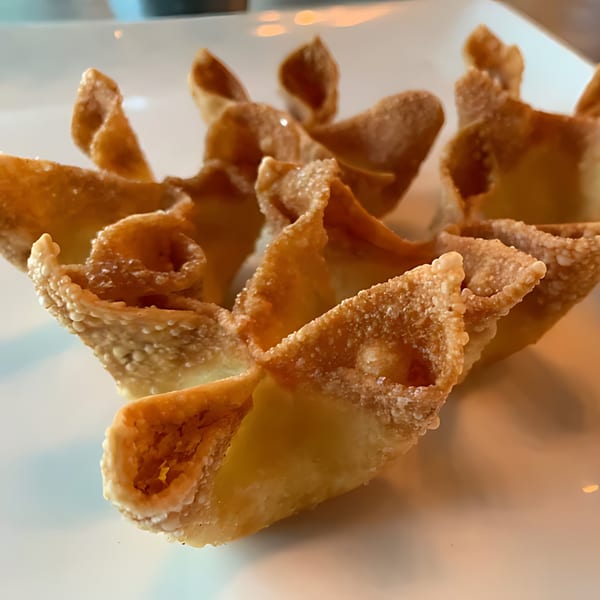 Close-up of several golden-brown, crispy crab rangoon on a white plate.