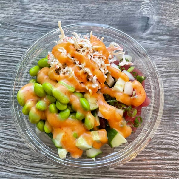 A vibrant poke bowl from Ye's Poke Station, topped with edamame, cucumber, crab salad, and orange sauce.